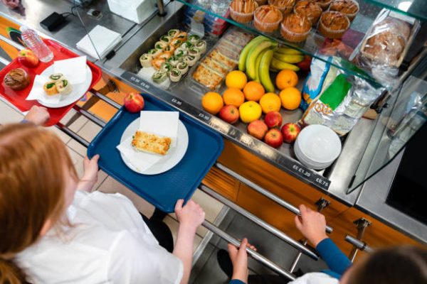 A high angle view of a young teenage girl who is looking at the options for her lunch in the school she goes to in the North East of England. There is plenty of choice of fresh fruit and snacks to choose from in the chiller cabinet.